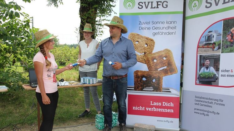 Alexander Apfelböck nutzt den SVLFG-Infostand, um eine seiner Saison-Arbeitskräfte mit einer Tube Sonnencremes auszustatten. Bild: SVLFG.