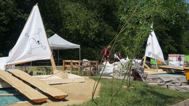 "Landschaftsgärtner-Cup Nord". Bild: Antje Kottich. Die Bauaufgabe war das Herzstück des Berufswettkampfes der Landschaftsgärter:innen. Innerhalb von zehn Stunden mussten alle elf Teams einen identischen Garten nach Plan bauen. Dieser stand ganz im Zeichen des Inselparks und bildete neben Ruinenteilen der „Wilhelmsburg“ auch ein angreifendes Piraten-Floß mit Gangway und eine stilisierte Fluss-Szenerie aus blauem Glasbruch und blau blühenden Pflanzen ab. Bild: Antje Kottich.